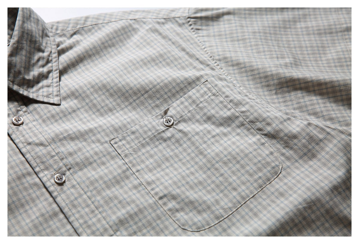 Close-up of a beige plaid shirt's pointed collar and buttoned chest pocket.