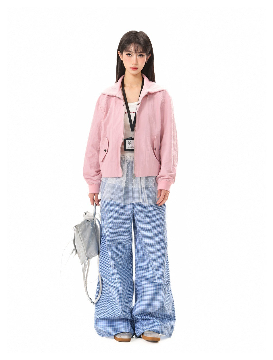 Model wearing pink cropped zip jacket over a white top with blue plaid wide-leg pants and a silver bag