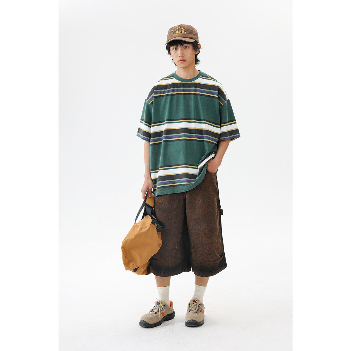 Model wearing an oversized green T-shirt with cream, navy and yellow horizontal stripes, brown shorts and a brown cap.