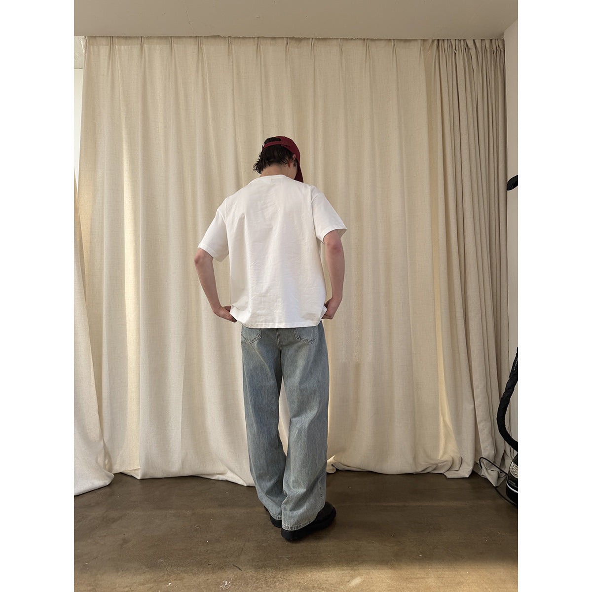 Back view of a model wearing a plain white T-shirt and loose light-wash jeans with a burgundy cap.