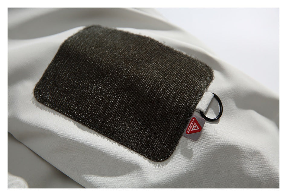 Close-up of a dark rectangular fabric patch and metal ring on a white jacket, with a small red tag.