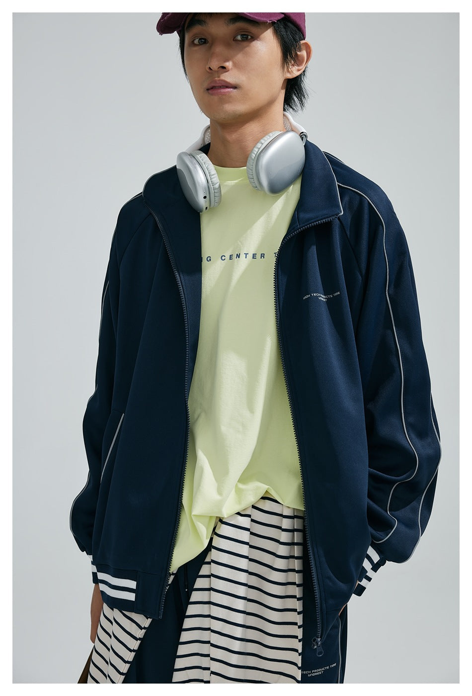 Close view of a model wearing an open navy track jacket with white piping and striped trim.