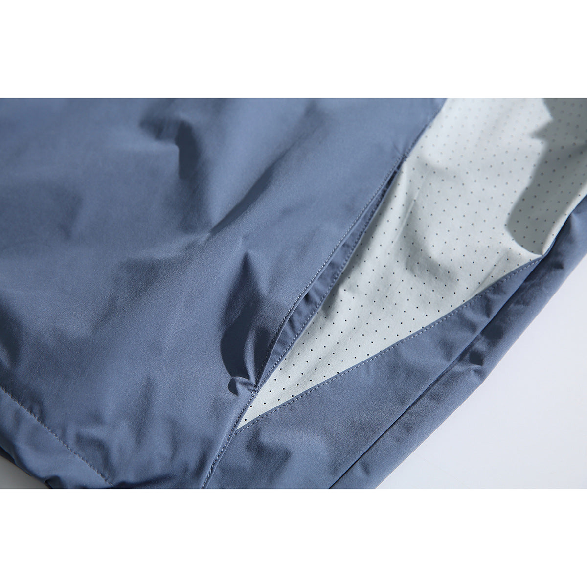 Close-up of the pullover's pale perforated side panel between slate-blue fabric sections.