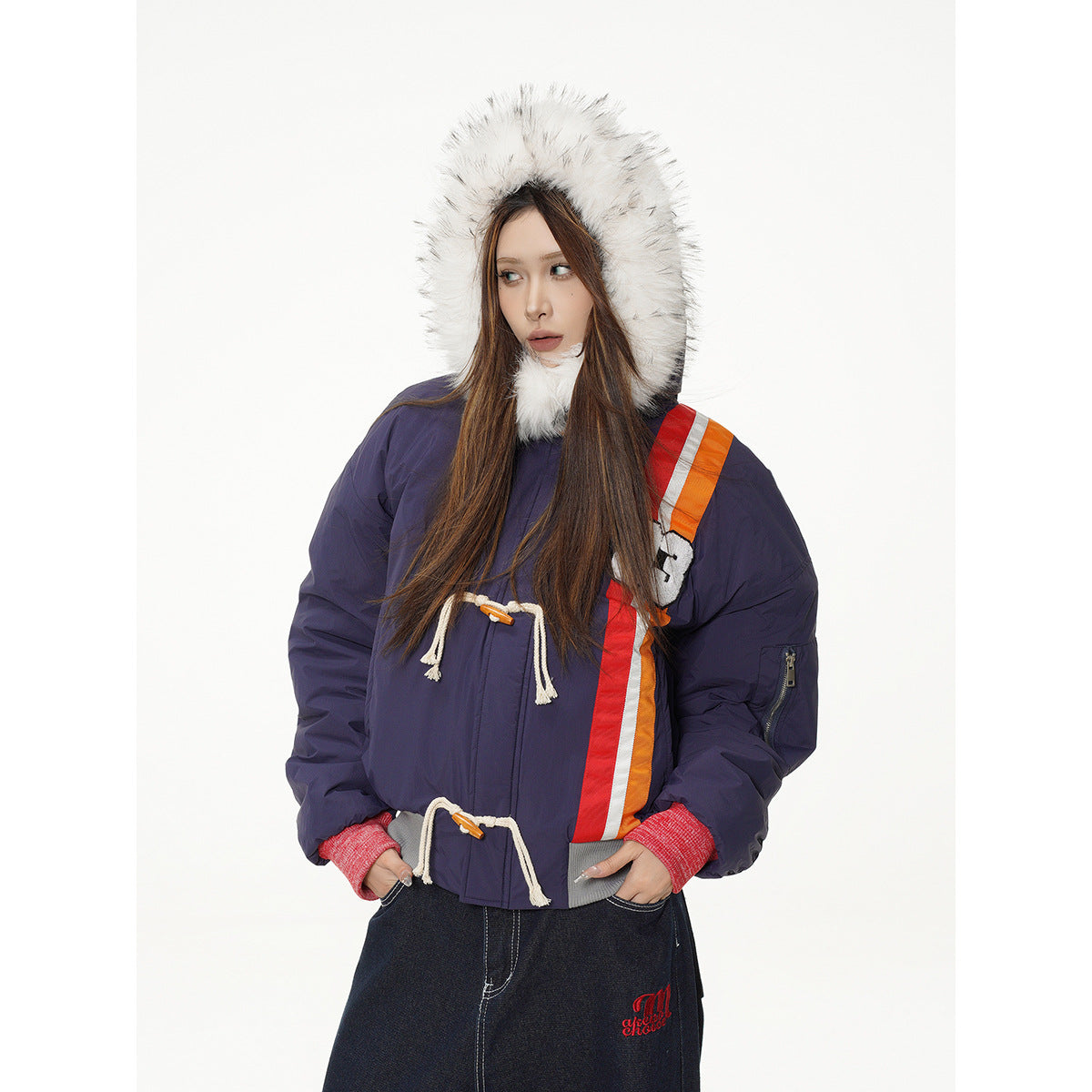 Model wearing a navy fur-trimmed hooded jacket with red and orange side stripes, shown from the front.