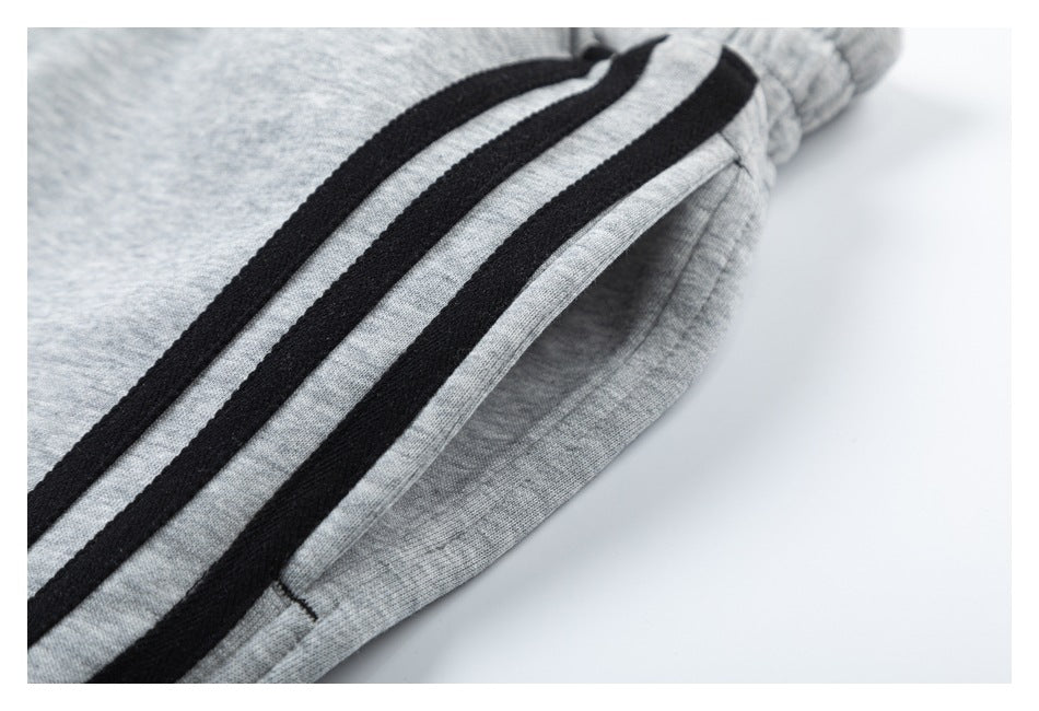 Close-up of light gray pants showing three black side stripes beside a pocket opening.