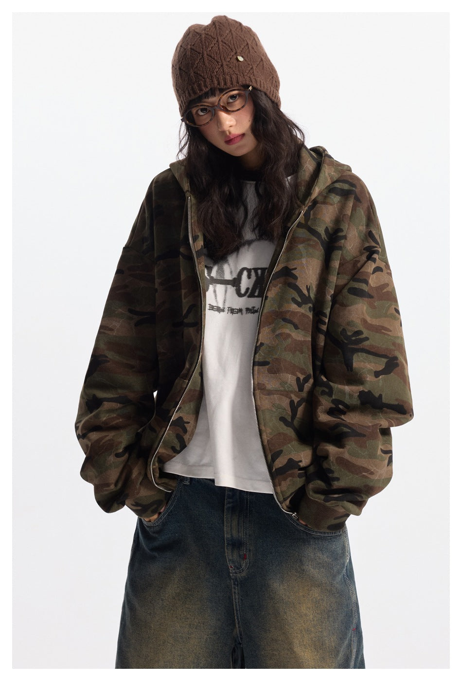 Model in a front view wearing an open oversized camouflage zip hoodie over a white graphic tee.