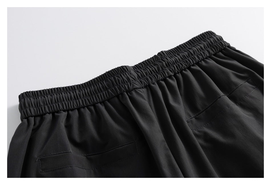 Close-up of black pants with a gathered elastic waistband and two rear welt pockets.