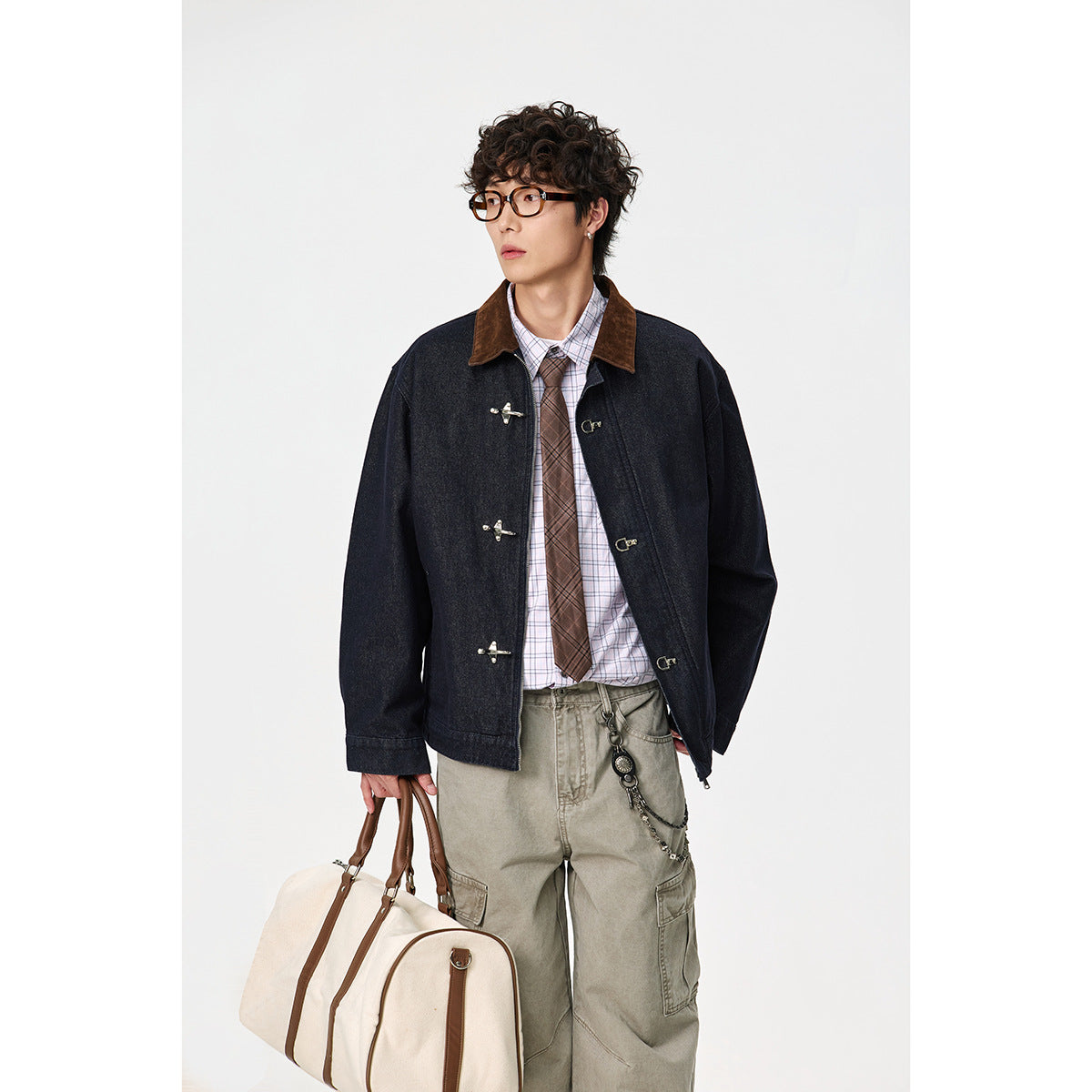 Model wearing a dark indigo jacket with a brown collar and silver toggle closures, paired with a plaid shirt and khaki cargo