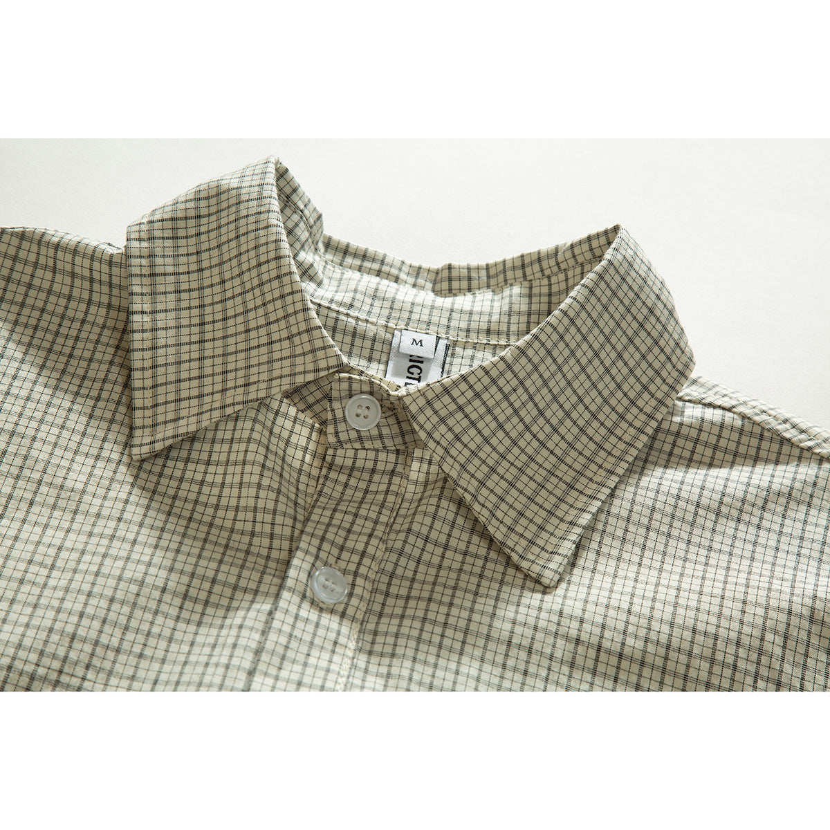 Close-up of a cream plaid shirt collar with white buttons and a partially visible neck label.