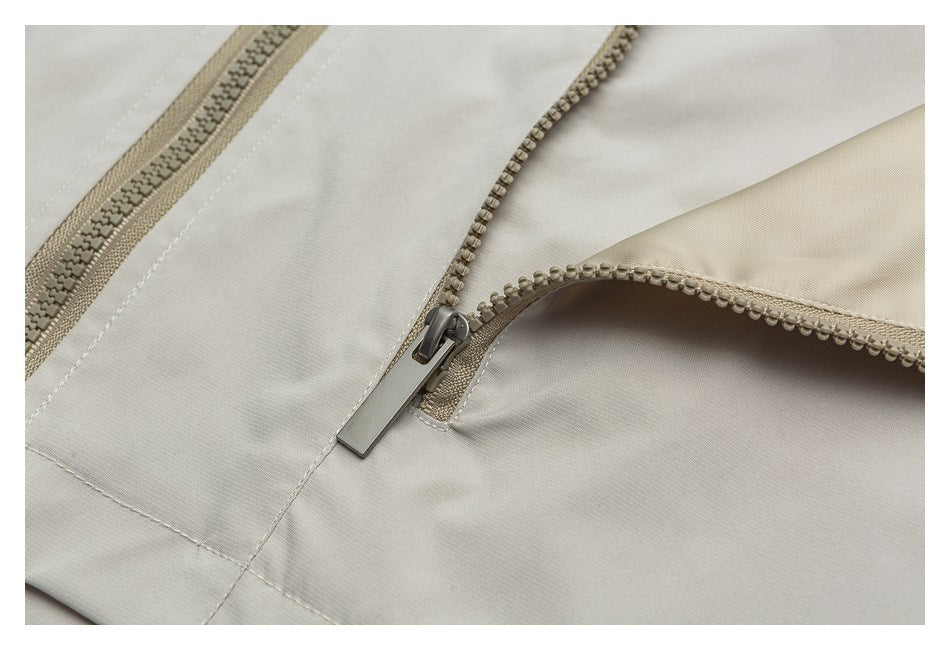 Close-up of a metal zipper pull and tan zipper teeth on light beige garment fabric.