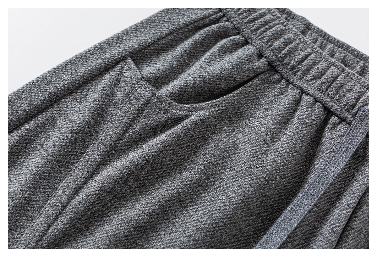 Close-up of heather gray joggers showing a curved pocket opening below the elastic waistband.