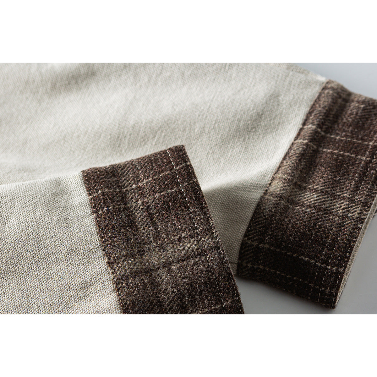 Close-up of a beige shirt sleeve finished with a dark brown plaid cuff.