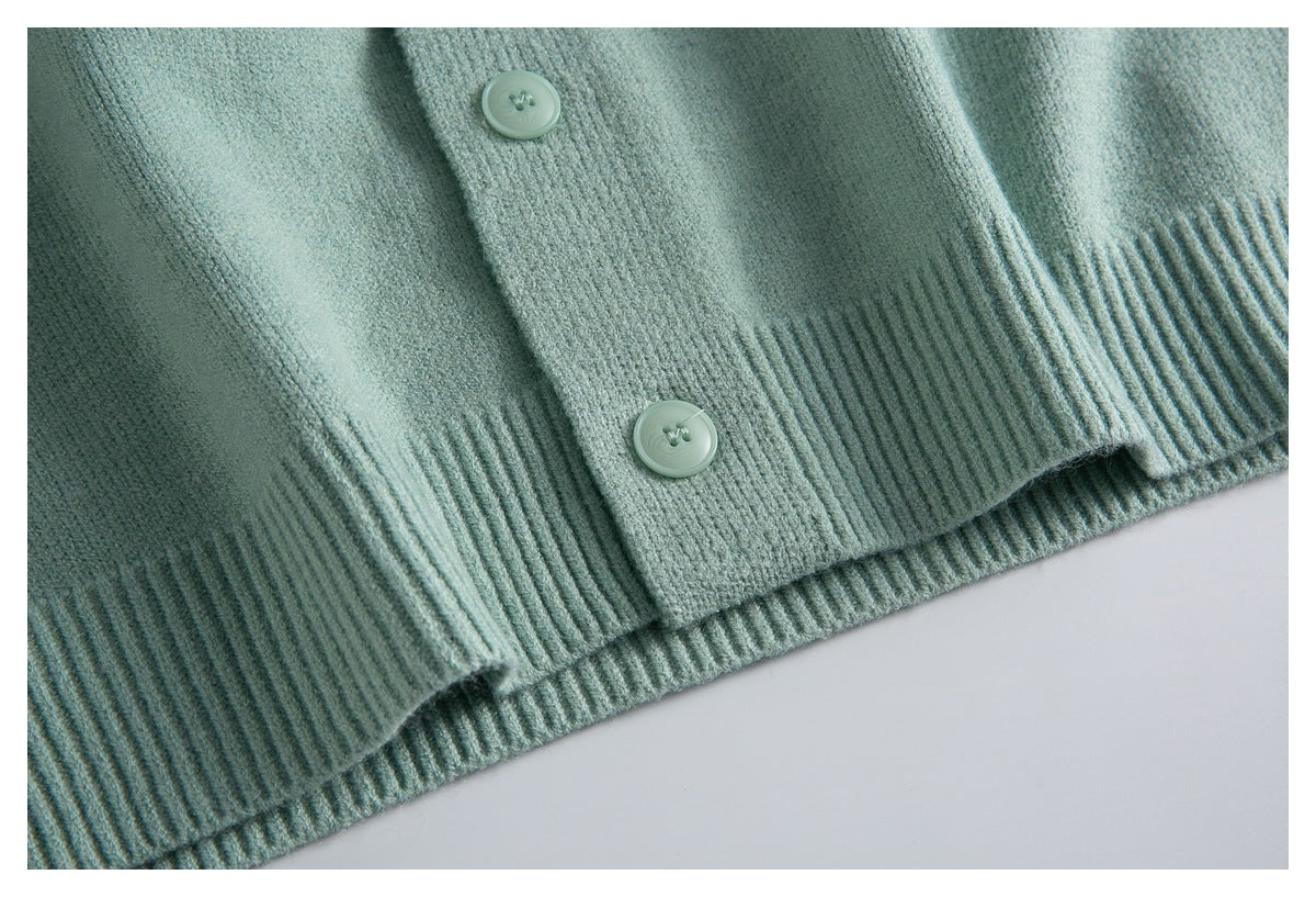 Close-up of a pale sage-green cardigan showing two buttons, the front placket, and ribbed hem.