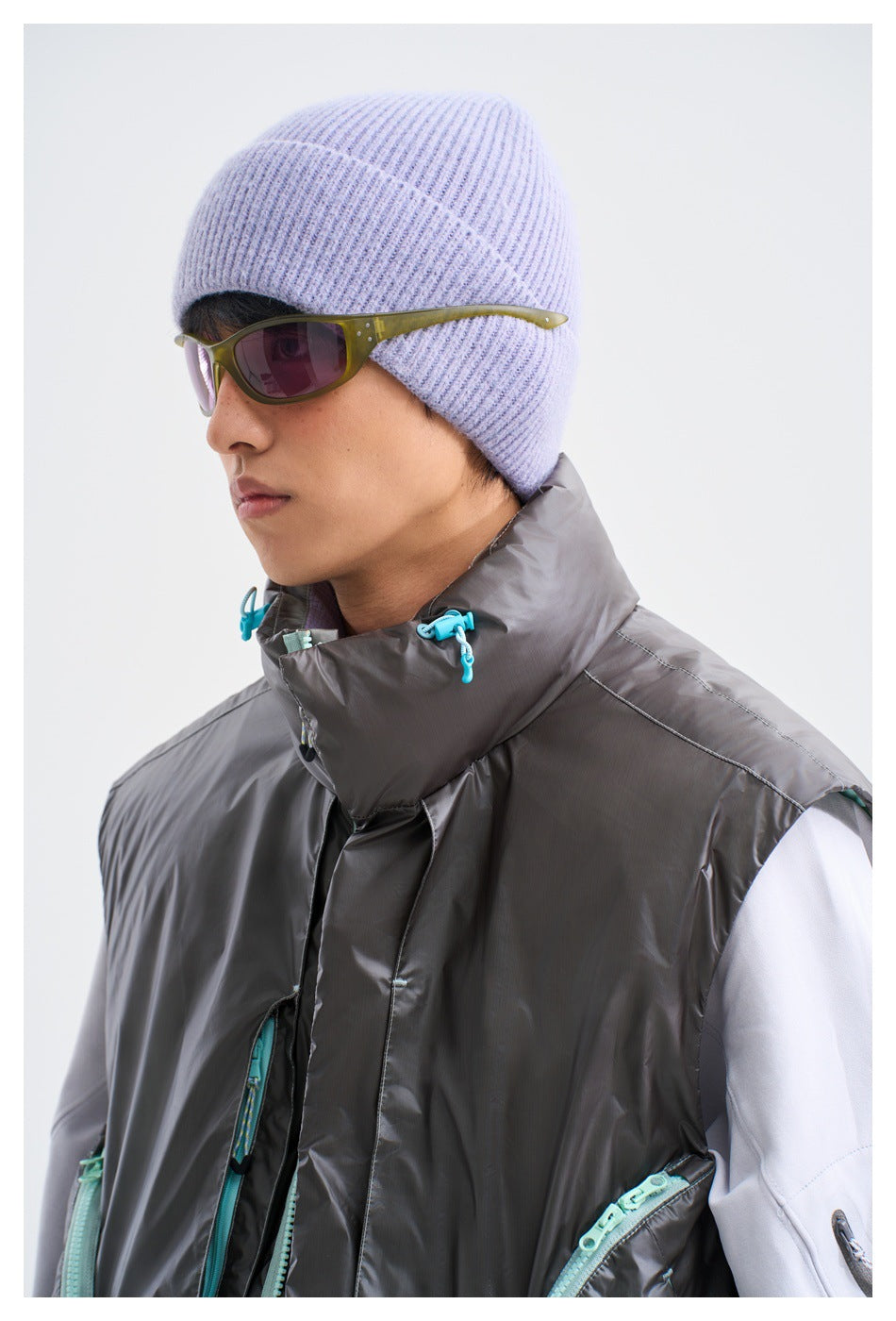 Close-up of a model wearing a charcoal-gray vest with a tall drawcord collar and turquoise zipper details.