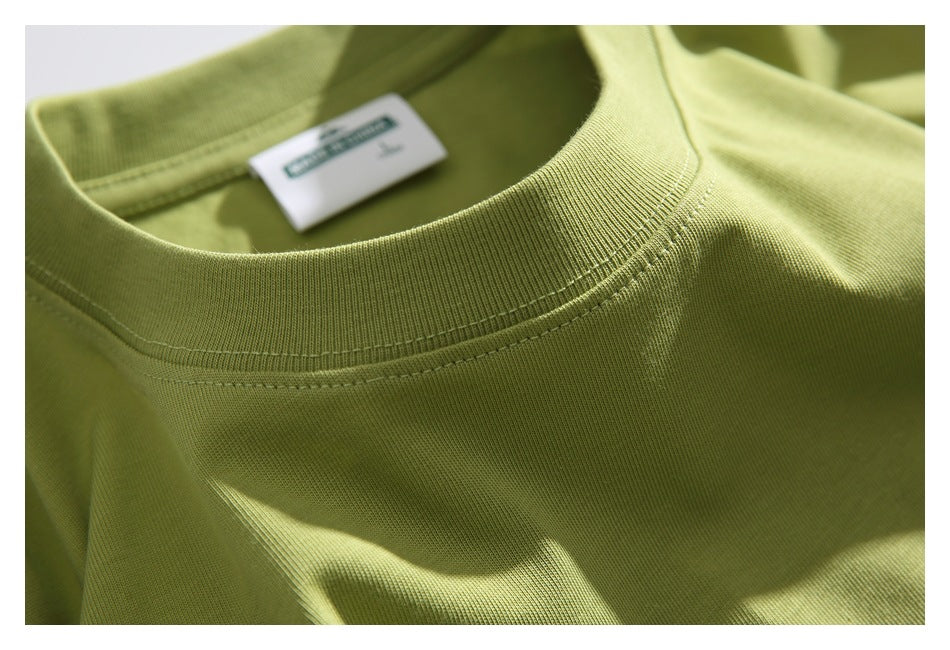 Close-up of the ribbed crew neckline and inner label of a light olive-green T-shirt.
