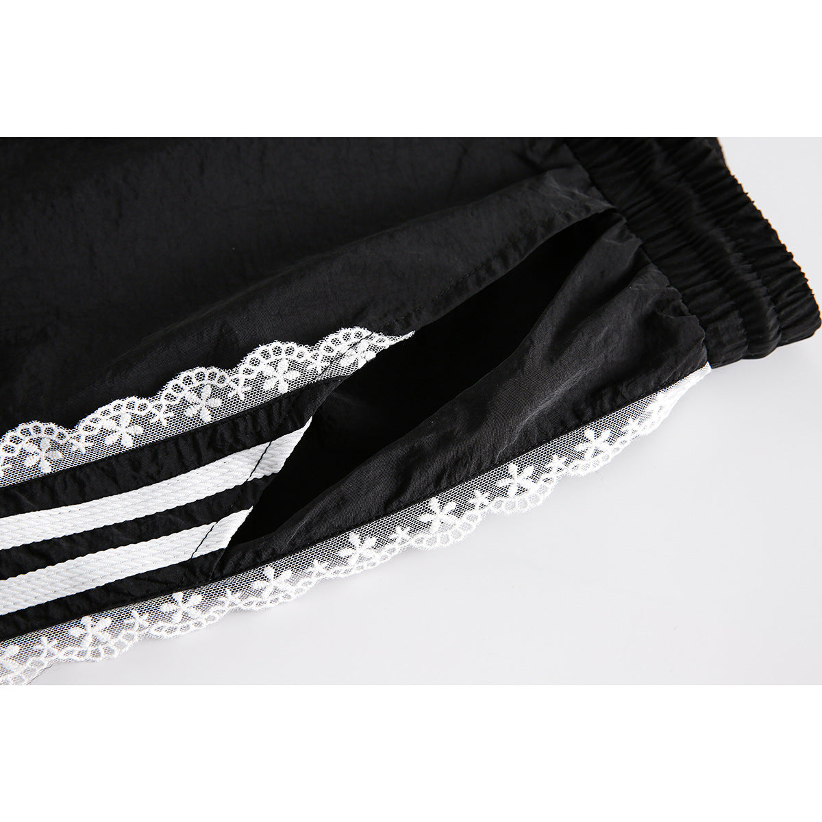 Close-up of a pocket opening and white floral-lace trim with stripes on black pants.