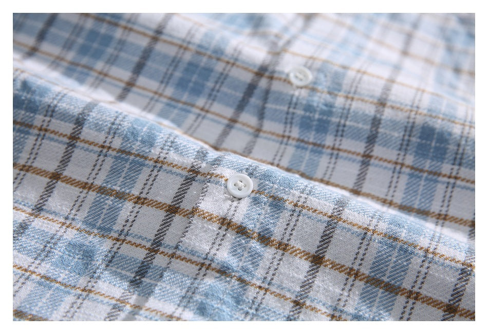 Close-up of a white button against the light blue, gray, white, and tan plaid shirt fabric.