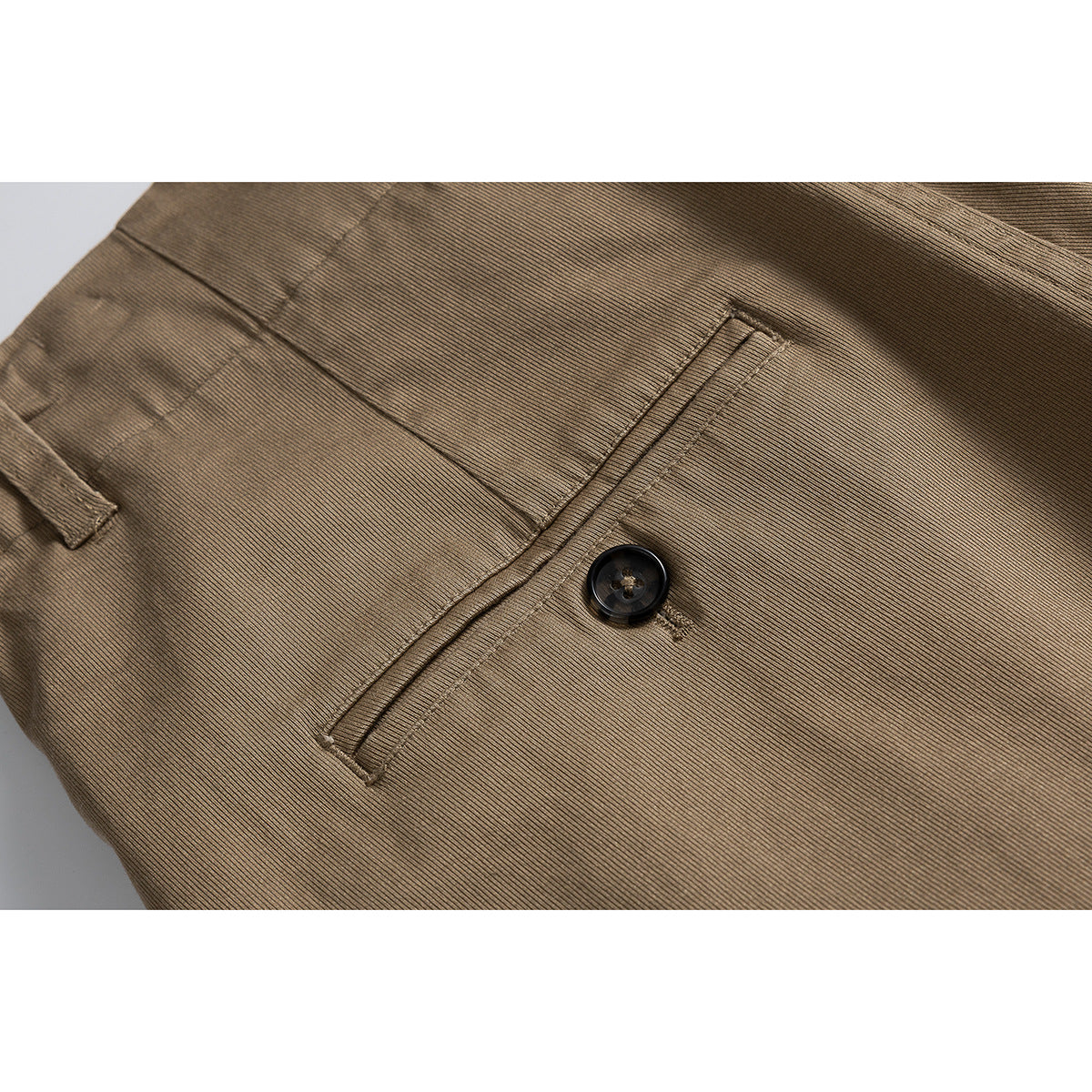 Close-up of tan shorts showing a welt pocket, dark button and fine ribbed fabric texture.