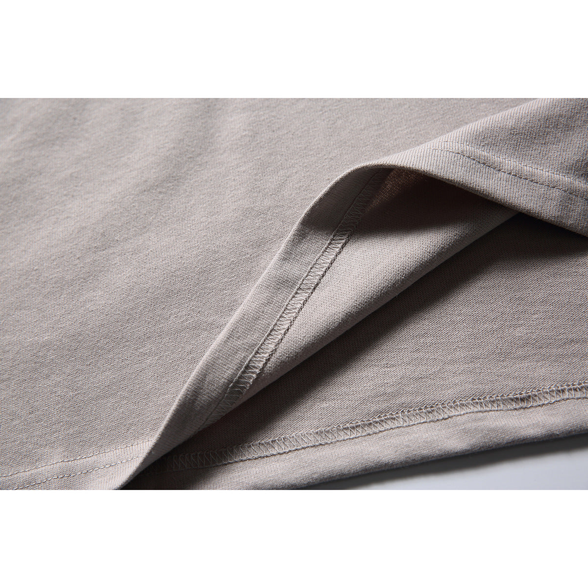 Close-up of the light taupe T-shirt's folded fabric and stitched hem seam.