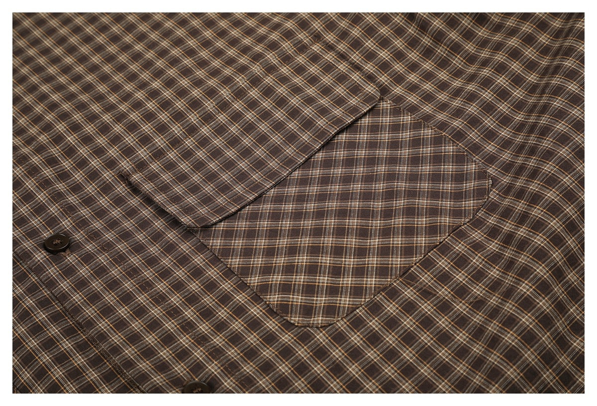 Close-up of a flap chest pocket on a brown plaid shirt, with the button placket partly visible.
