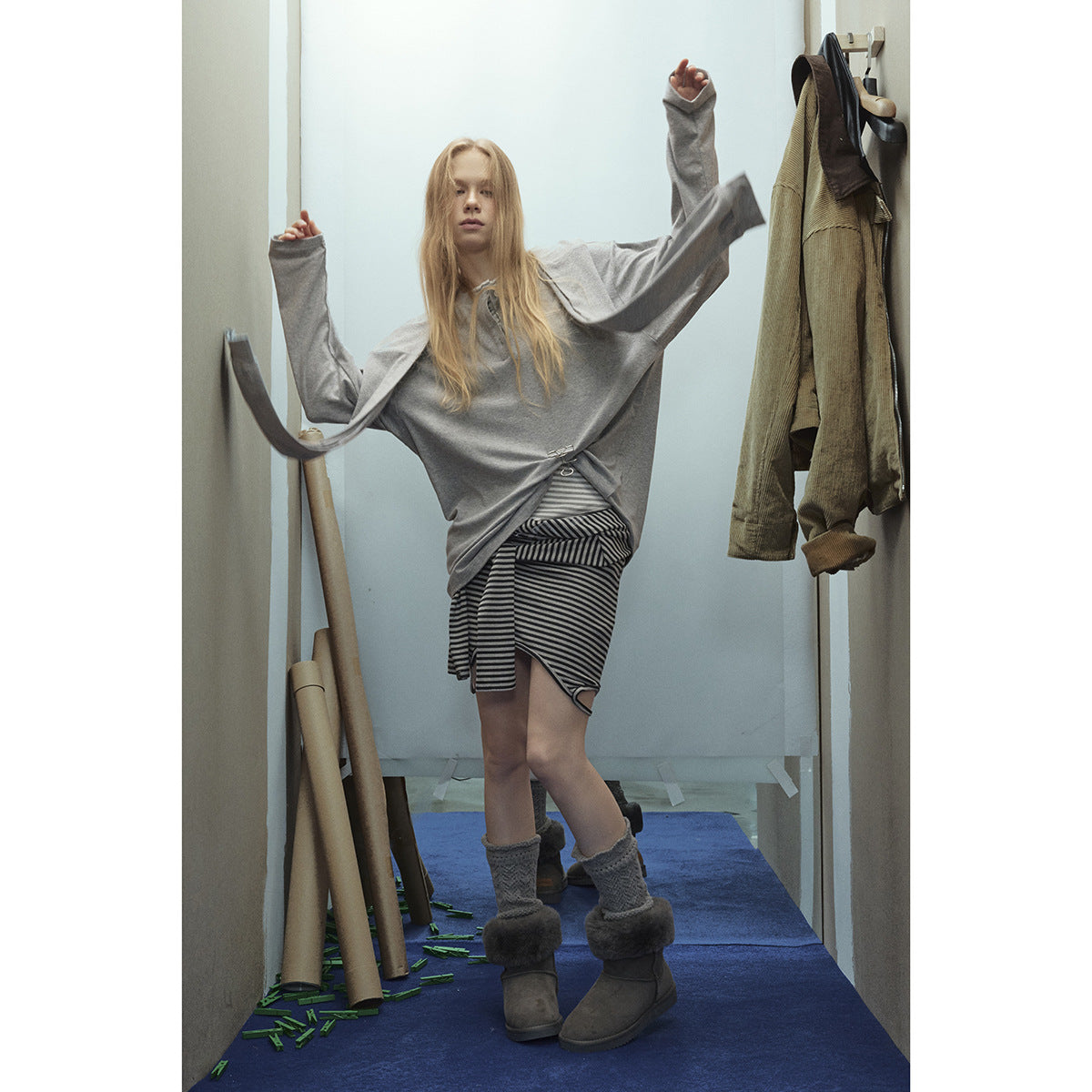 Model wearing an oversized gray long-sleeve top with a metal waist clasp and a black-and-gray striped wrap skirt.