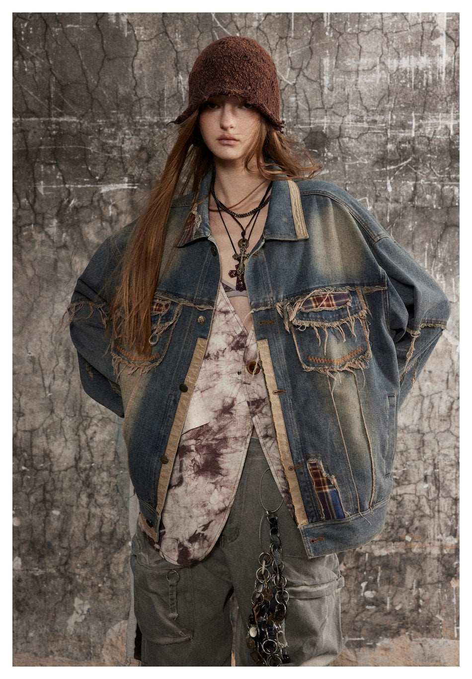 Model wearing oversized faded denim jacket with plaid patches and beige trim, styled with a brown knit hat