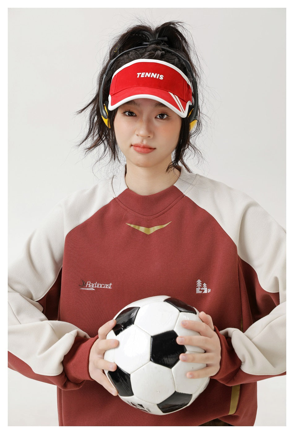 Close view of a woman wearing a rust-red and cream color-block sweatshirt and holding a soccer ball.