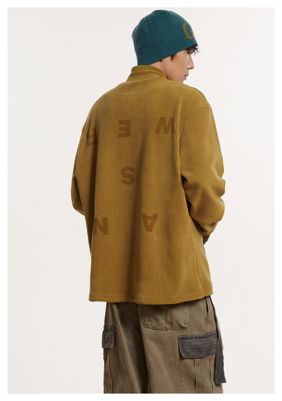 Rear view of a model in a mustard high-neck top with large scattered lettering across the back.