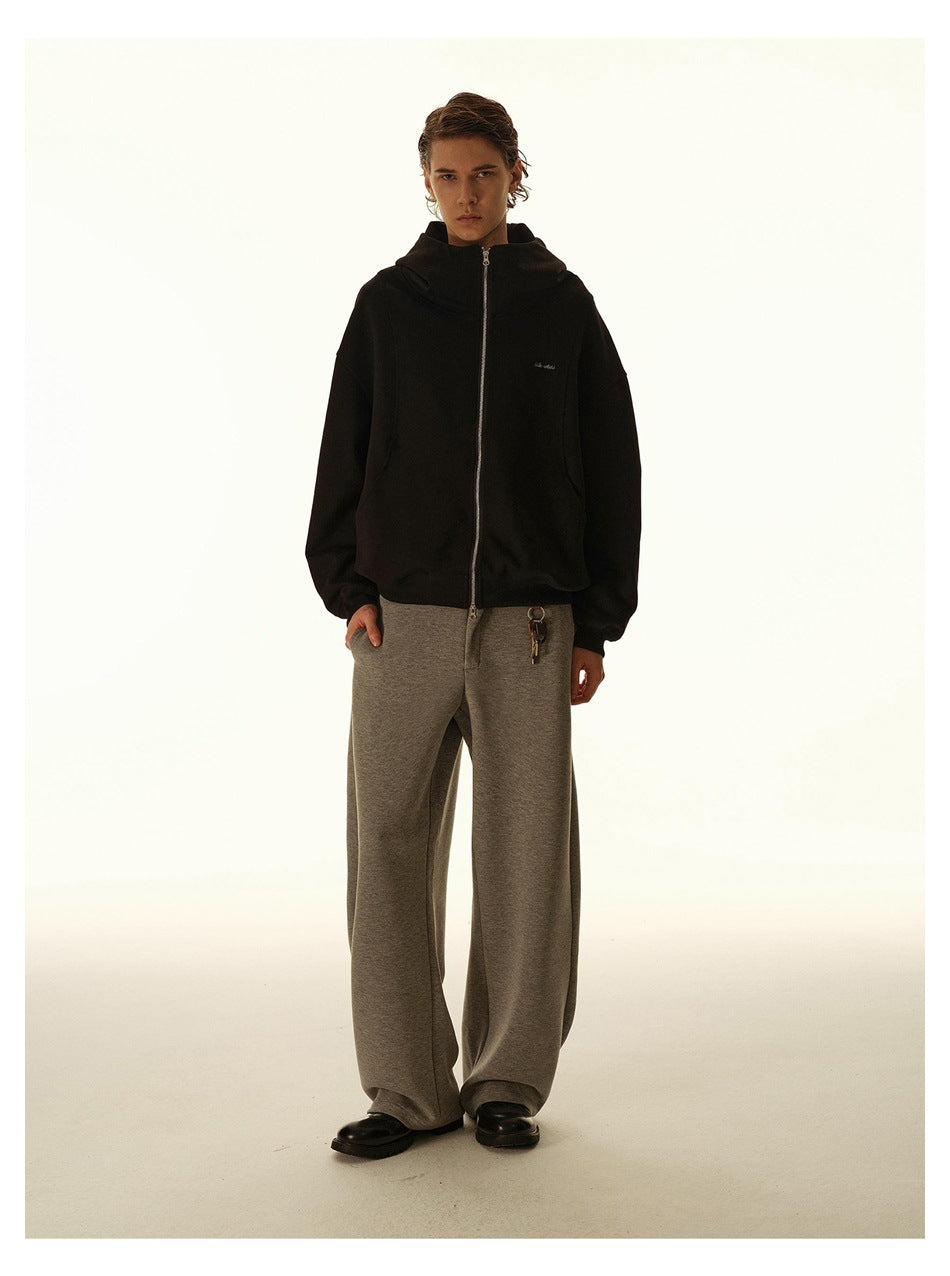 Front view of a model wearing a black zip-up hoodie with a hood and wide-leg gray pants.