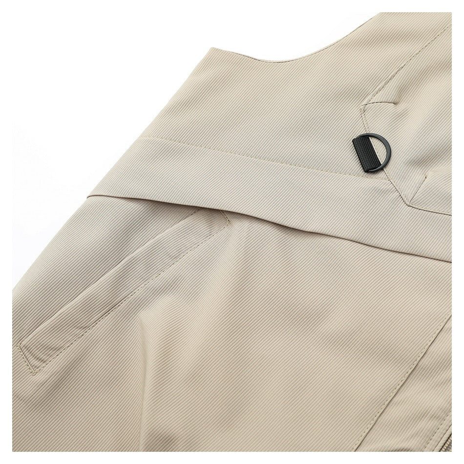 Close-up of the beige vest's layered panel, seam stitching, and black D-ring attachment.