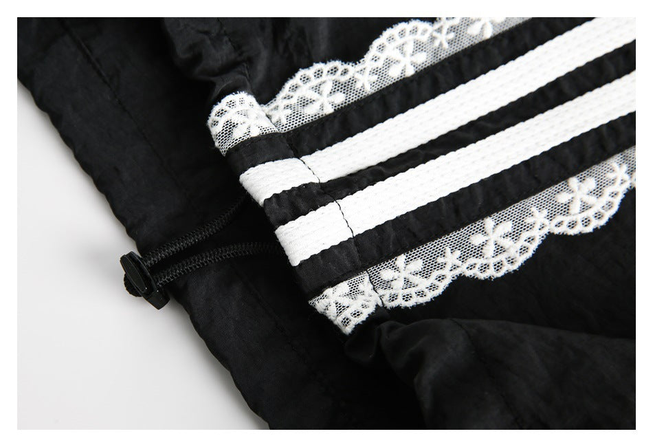 Close-up of a black zipper beside white stripes and floral lace trim on black fabric.