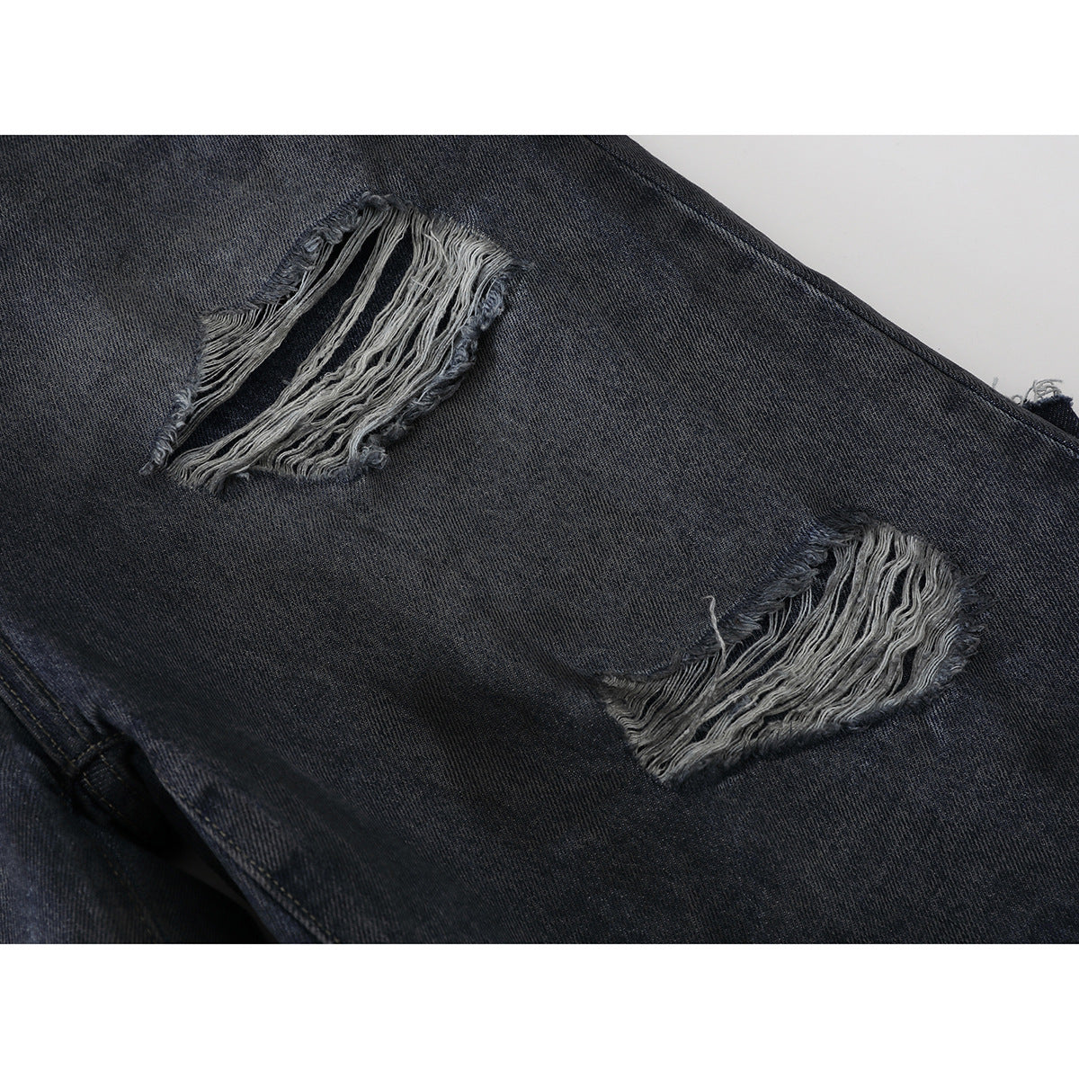 Close-up of two large frayed tears on dark charcoal denim.