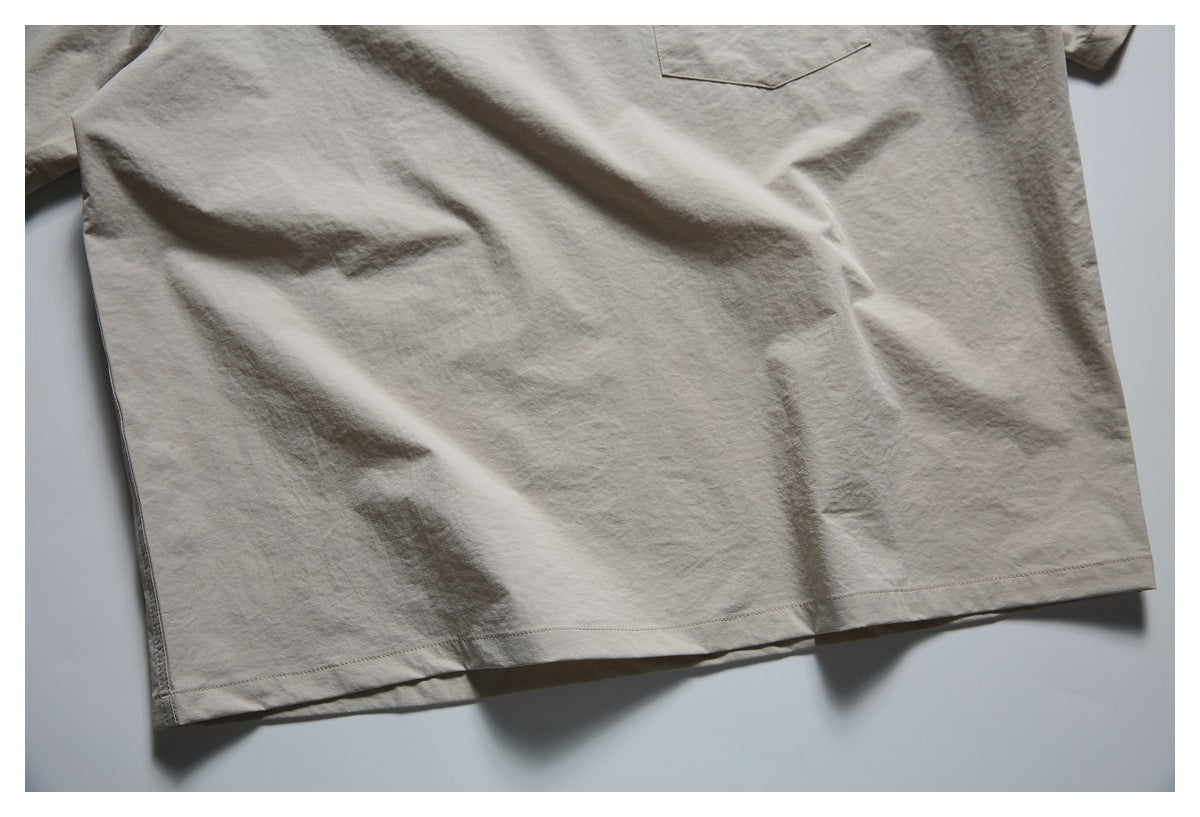 Close-up of the lower body and stitched hem of a light taupe shirt, with part of a pocket visible.