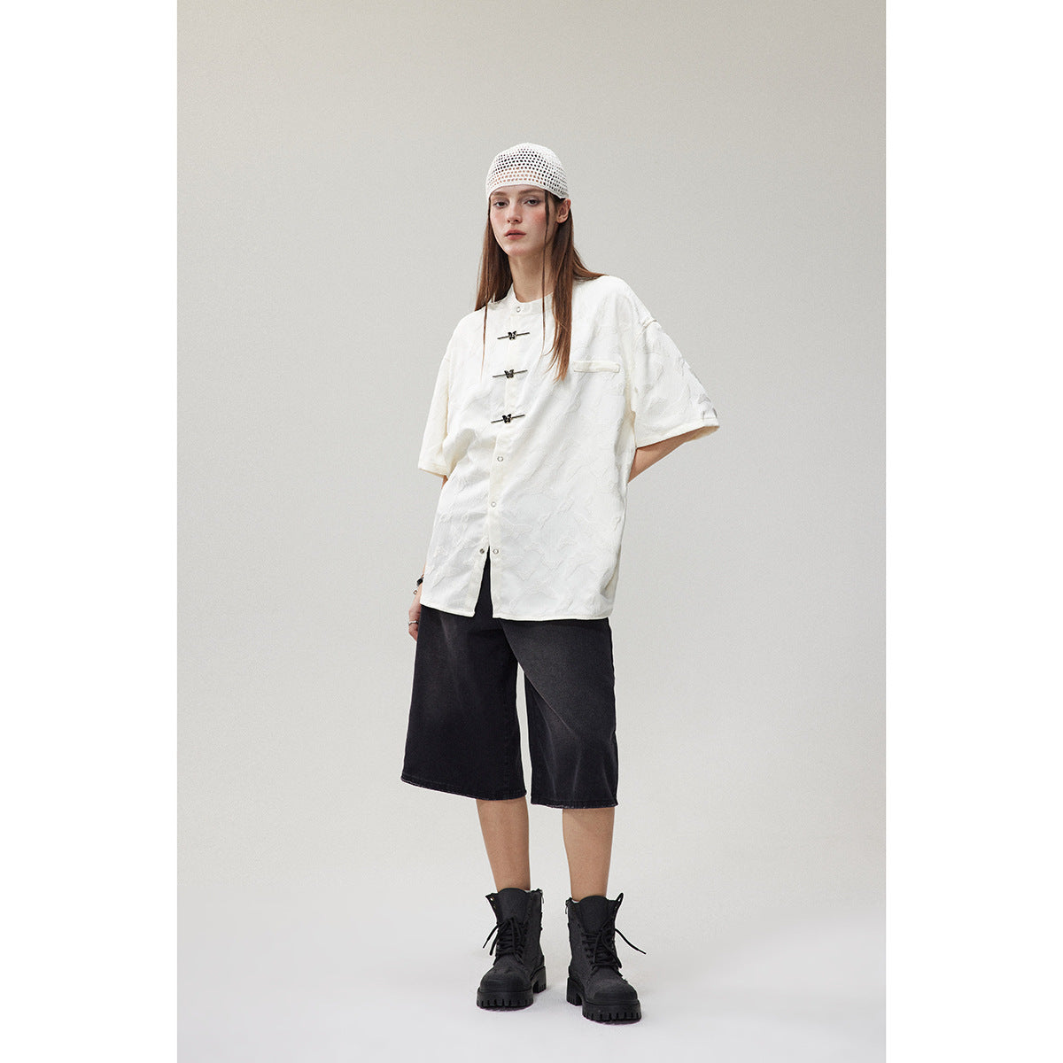 Model wearing a white short-sleeve jacquard shirt with frog closures and black wide-leg shorts.