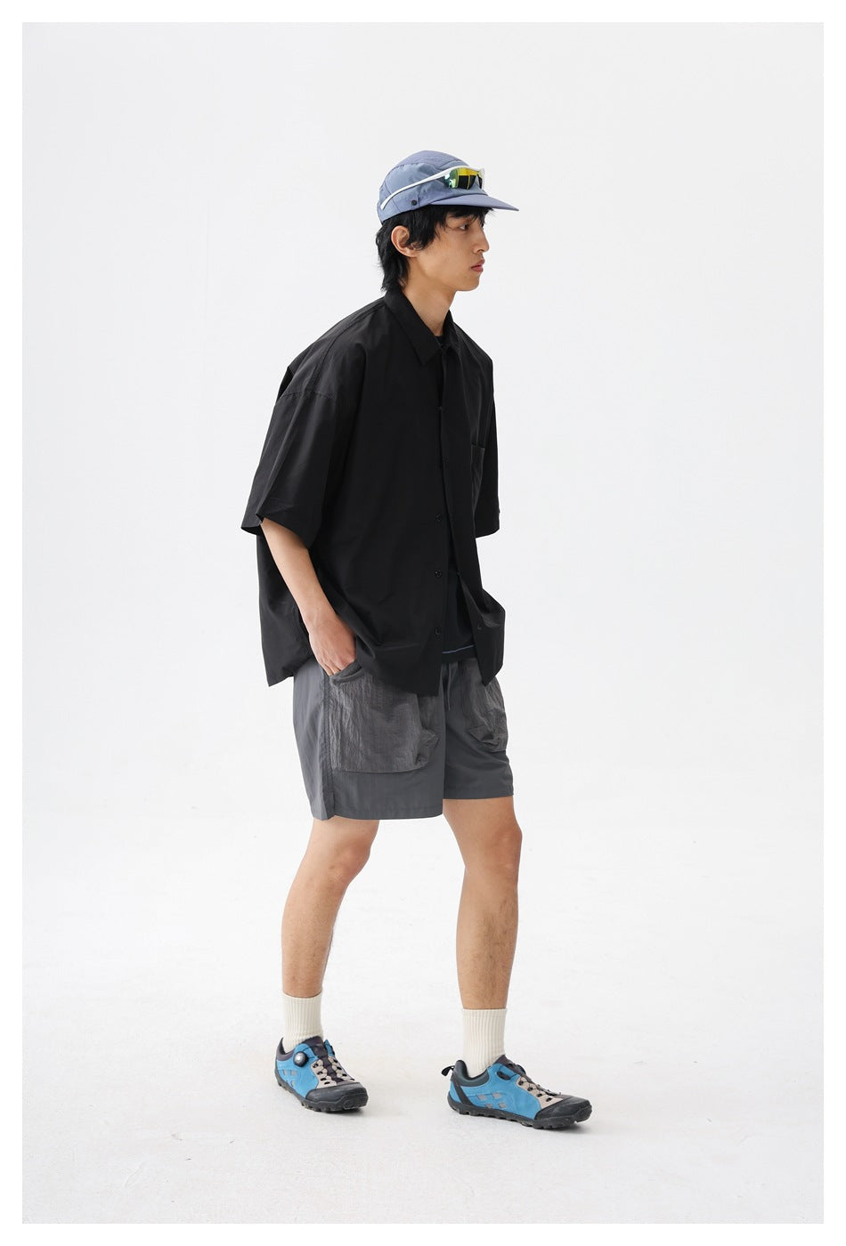Model wearing a loose black short-sleeve button-up shirt with a chest pocket, shown from the side.
