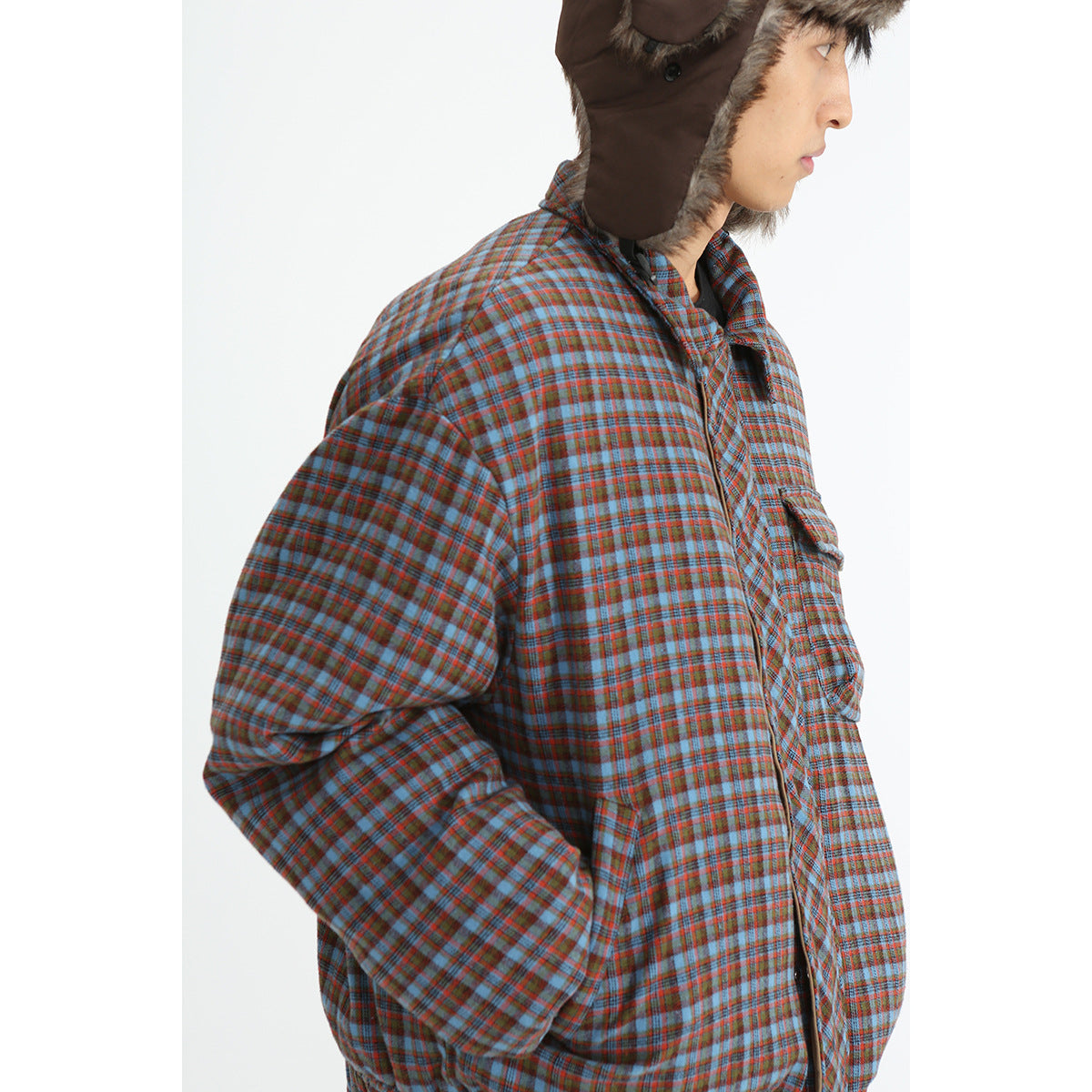 Side view of a person wearing a blue and rust plaid jacket with a brown fur-trimmed trapper hat.