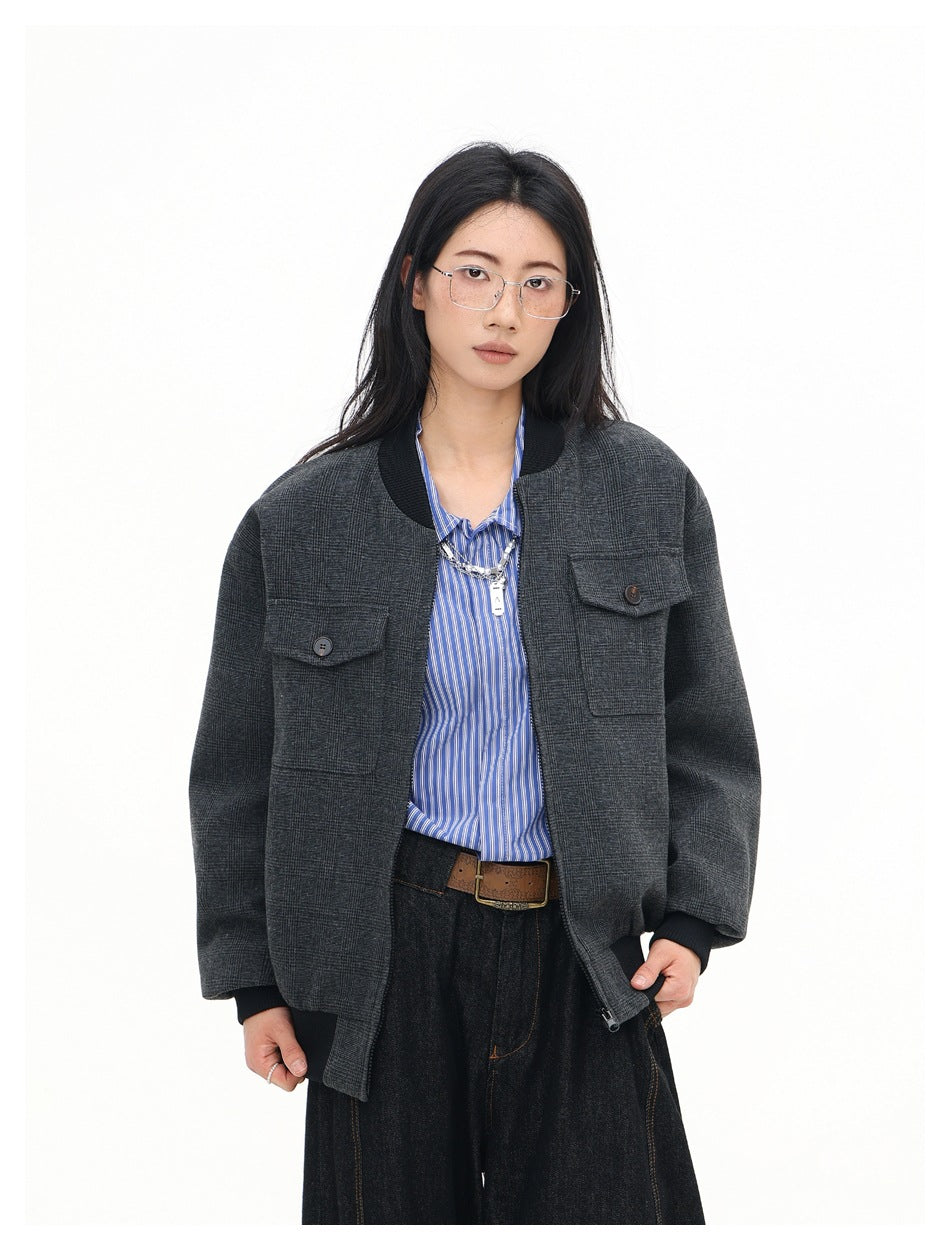 Closer front view of a model wearing a charcoal plaid bomber jacket with black ribbed trim and button-flap chest pockets.