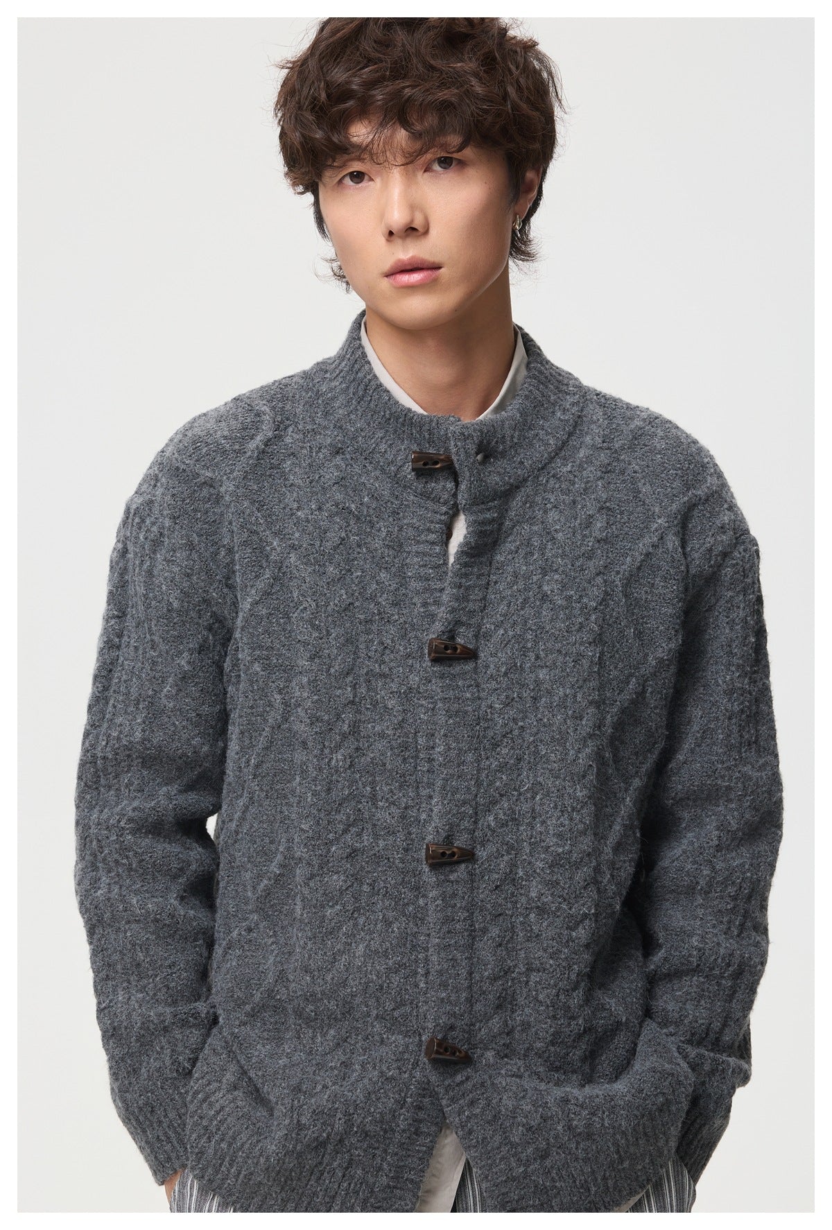 Close-up of a man wearing a dark gray cable-knit cardigan with brown horn-shaped toggle buttons