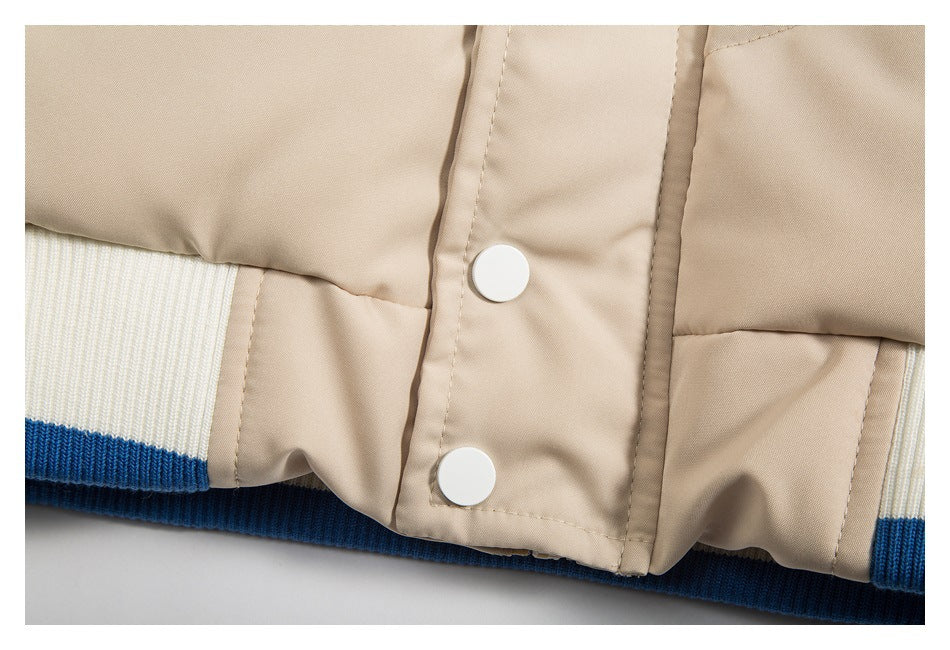 Close-up of two white snap buttons on the beige jacket’s front placket, above blue-and-white ribbed trim.
