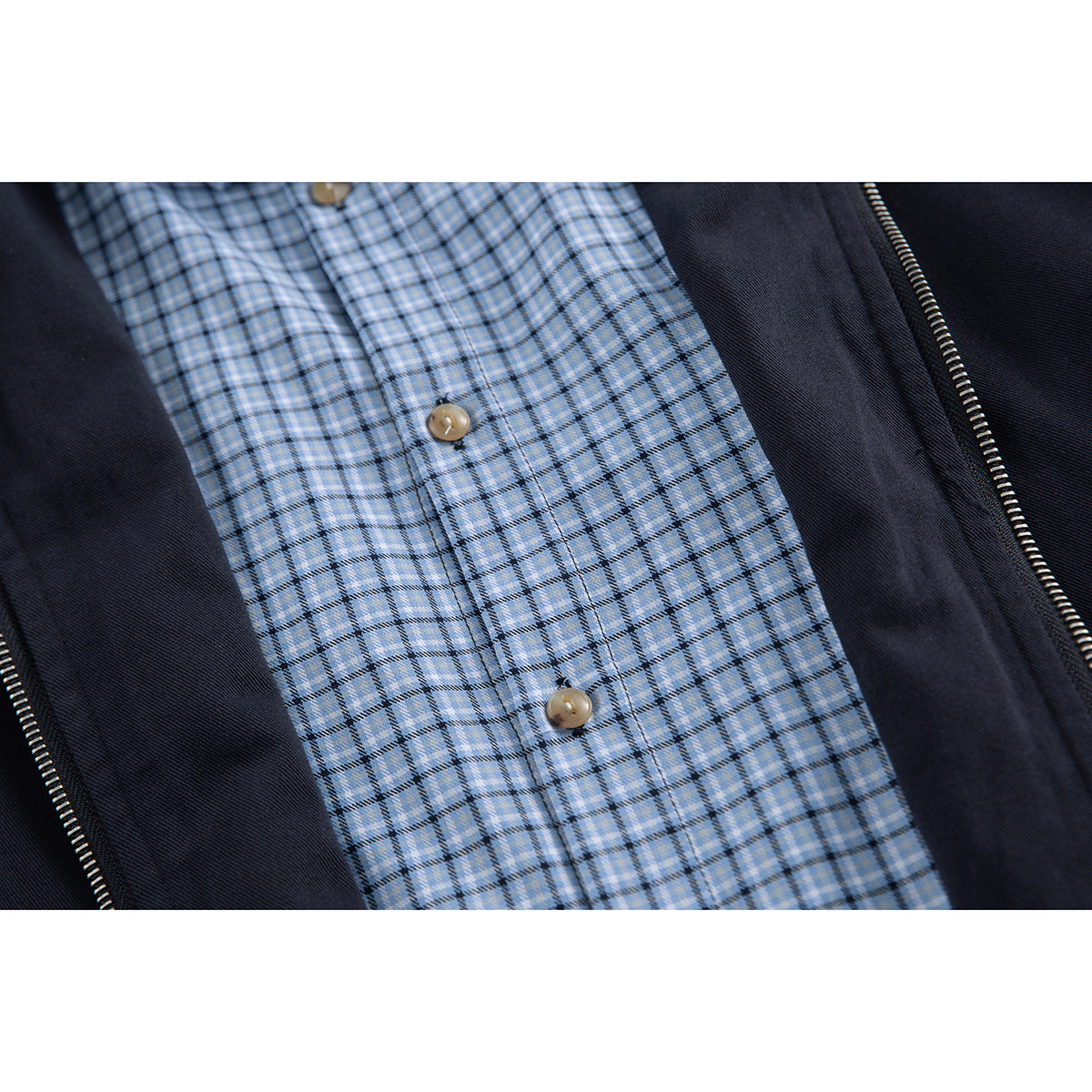 Close-up of a light blue plaid button-front layer framed by the open dark navy jacket and zipper.