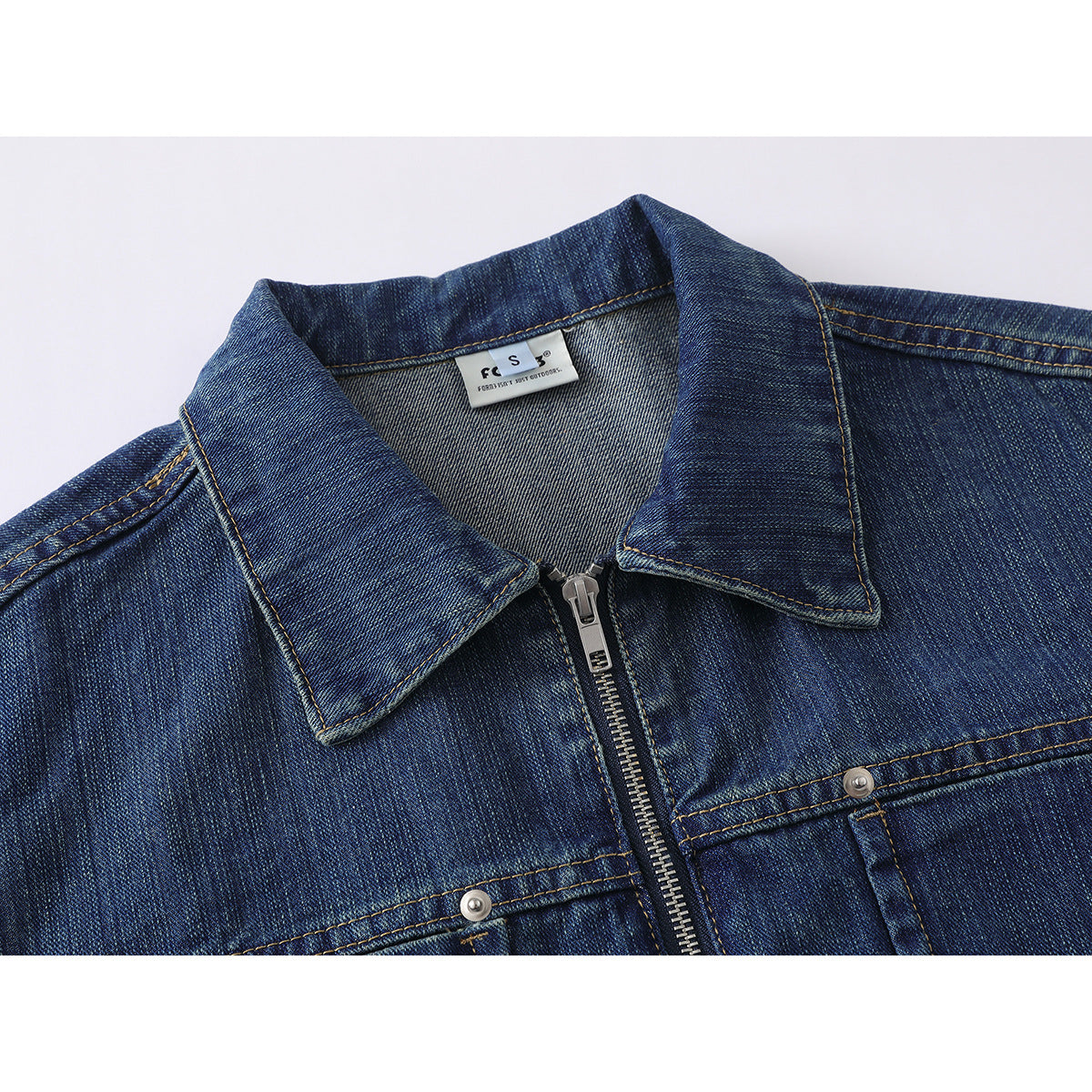 Close-up of a dark blue denim jacket collar, zipper, and upper chest pocket stitching.