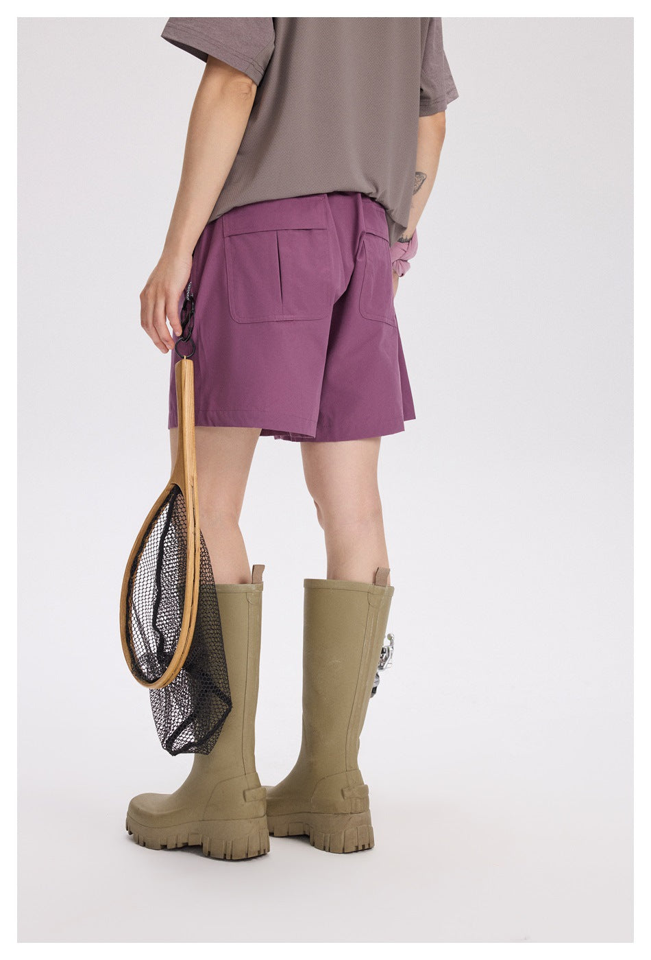 Rear view of a person wearing plum-purple shorts with two back pockets, a gray shirt, and khaki boots.