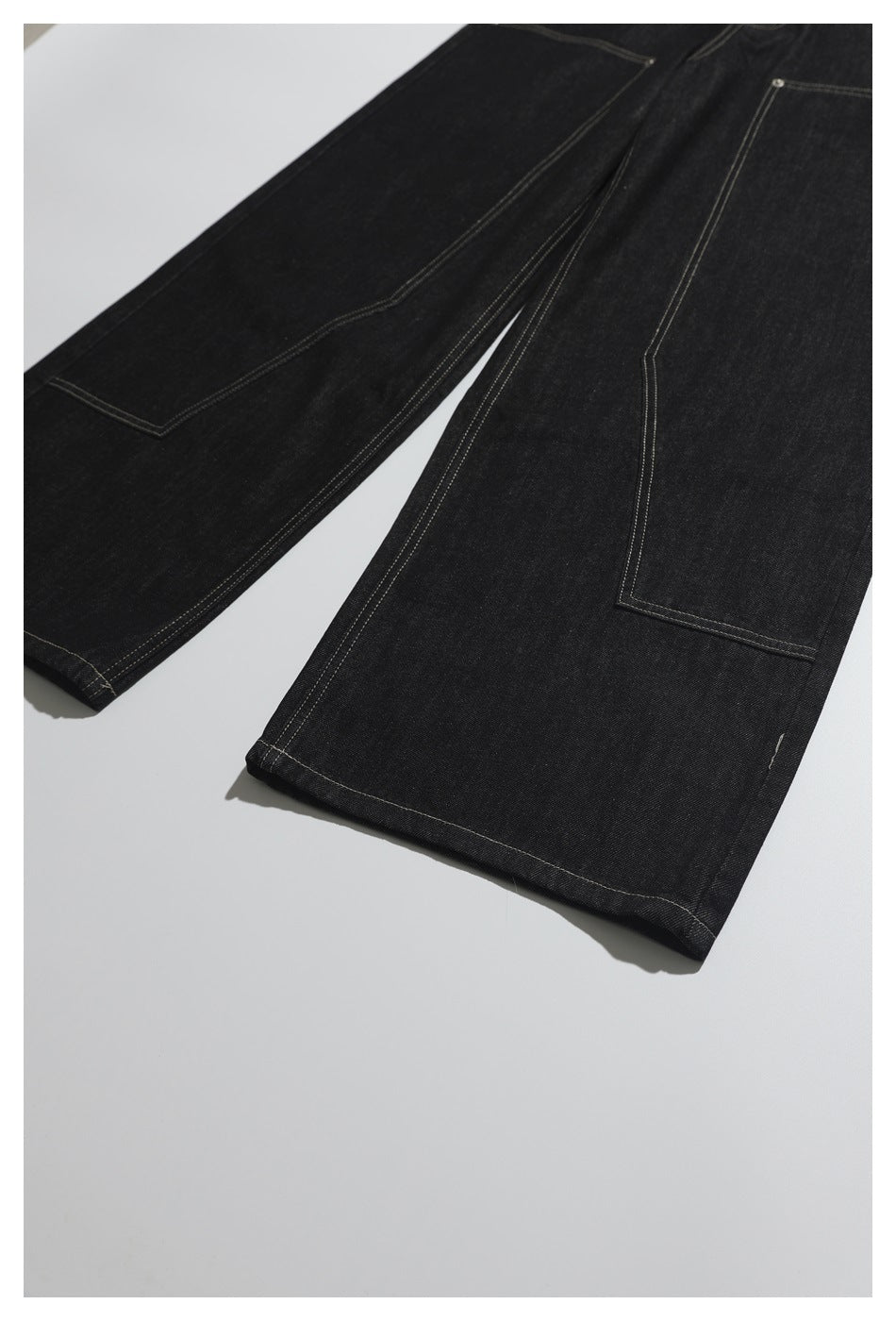 Close view of black jeans laid flat, showing long stitched patch pockets and straight hems.