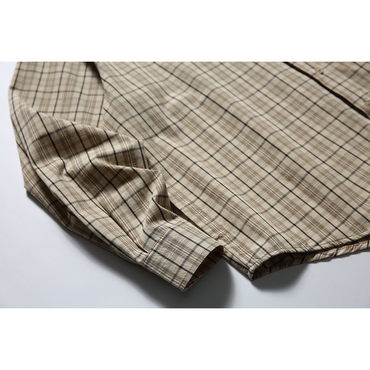 Close-up of the beige plaid shirt fabric gathered around a buttoned sleeve cuff.
