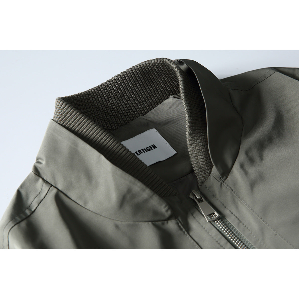 Close-up of an olive-gray bomber jacket collar, inner label, and metal front zipper.
