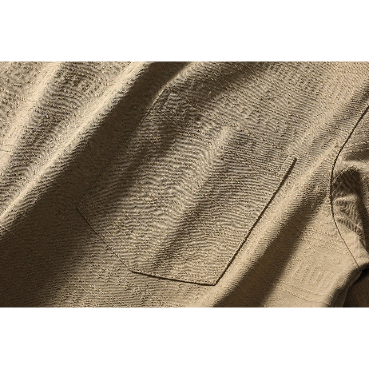 Close-up of the tan patterned shirt’s stitched chest pocket and short-sleeve seam.