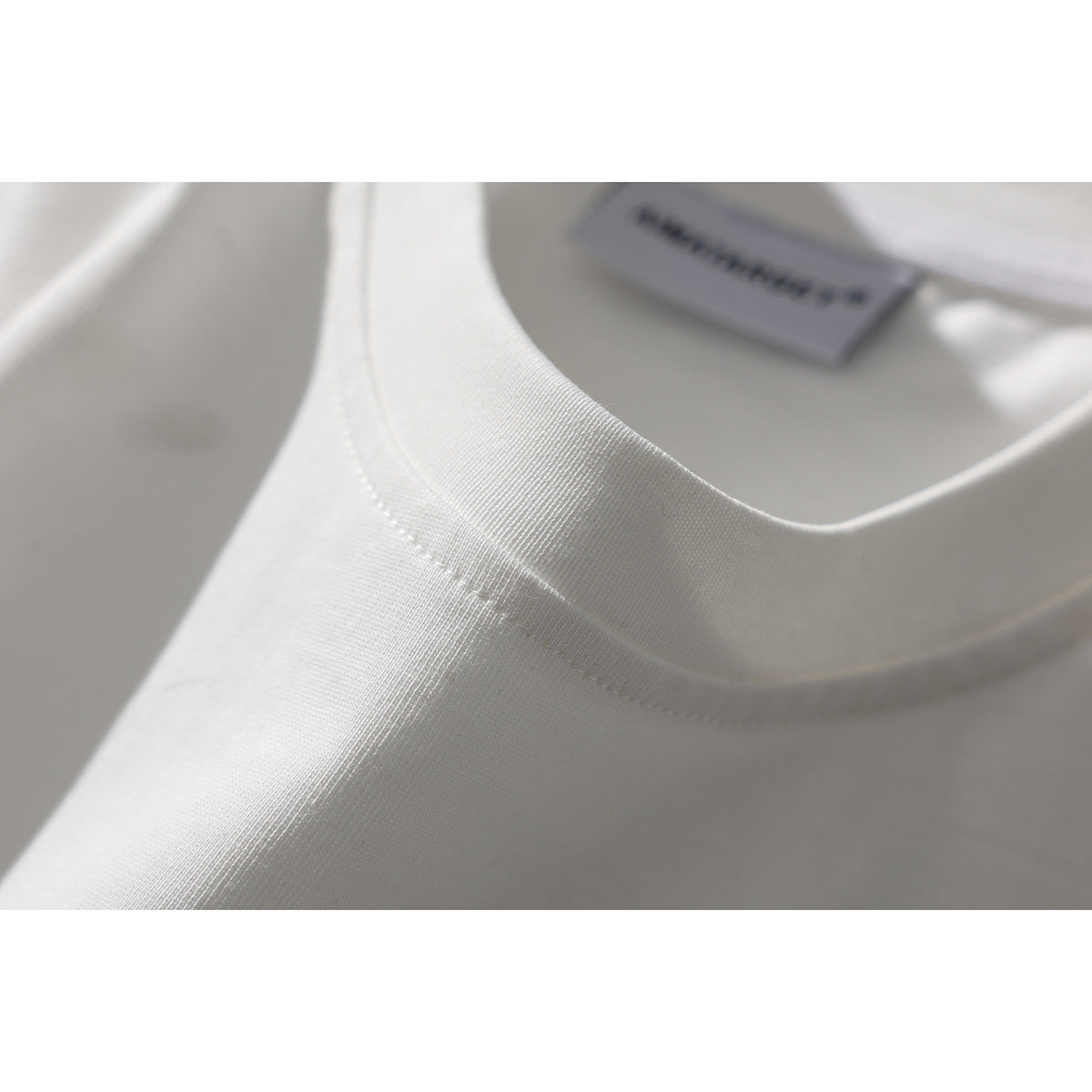 Close-up of a white T-shirt's ribbed crew neck and stitching, with a blurred inner label.