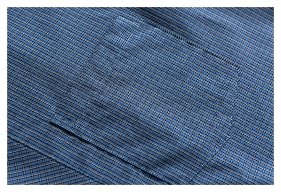 Close-up of a blue checked shirt showing a stitched chest pocket.