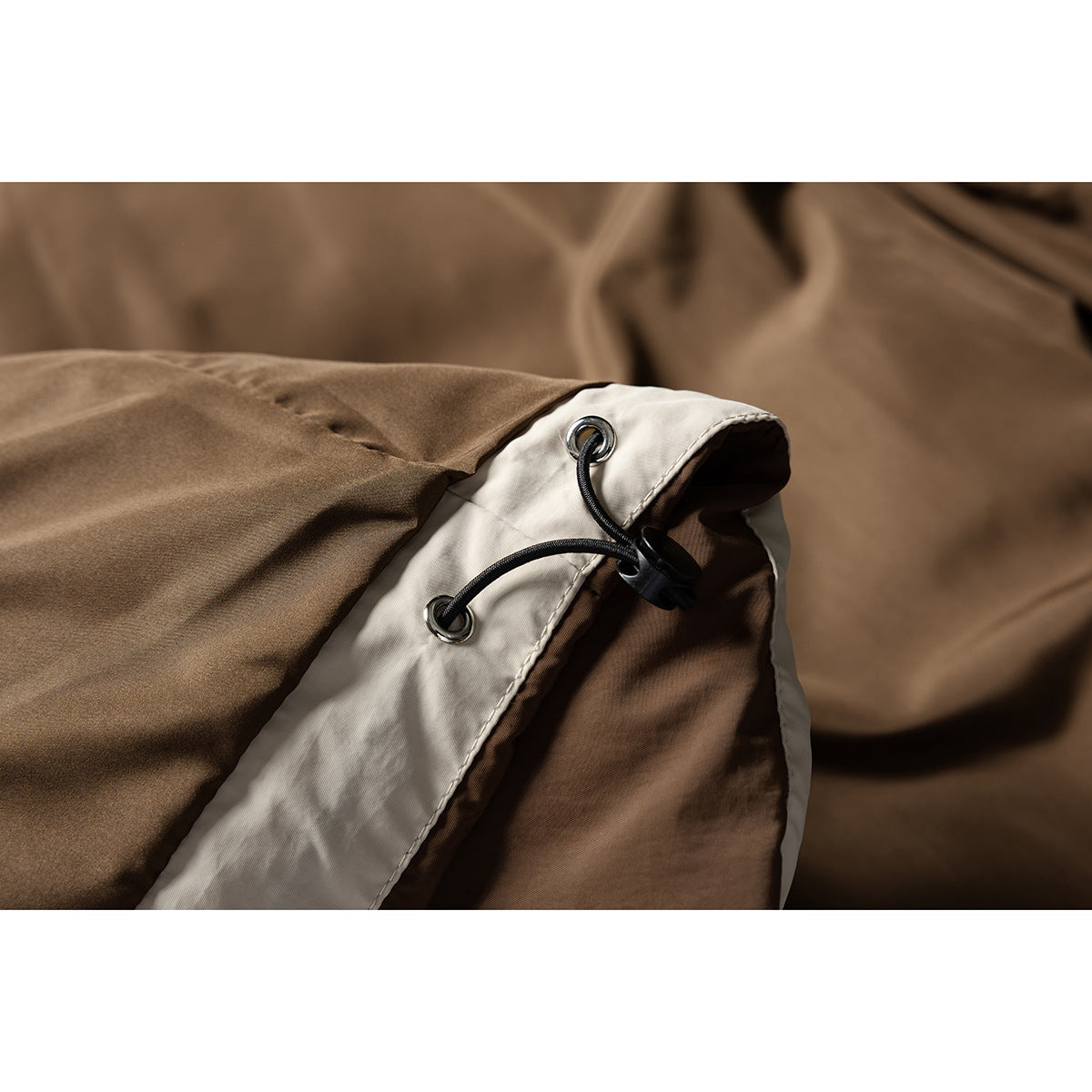 Close-up of a brown jacket with a cream panel, metal eyelets and a black adjustable drawcord.