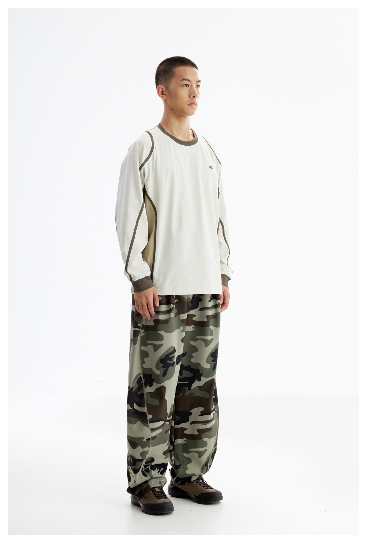 Model wearing an off-white color-block long-sleeve shirt with loose green camouflage pants, shown at a slight angle.